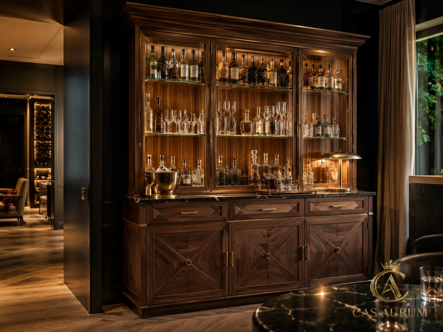 Walnut and glass bar cabinet with illuminated bottle display, brass hardware and dark stone counter by CAS AURUM.